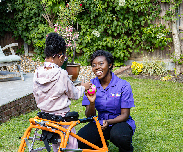 Prestige carer supporting a child using a walking frame outdoors