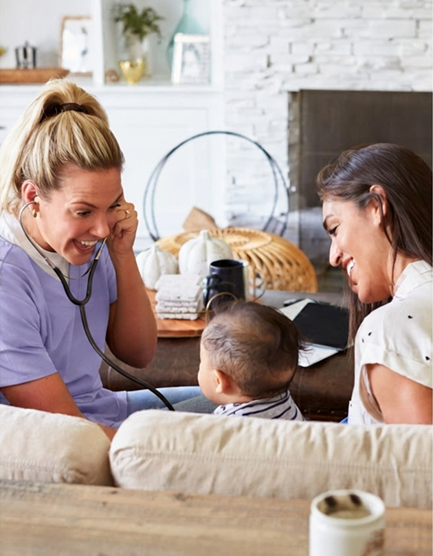 A woman sits on a couch with a baby, while another woman talks on the phone nearby