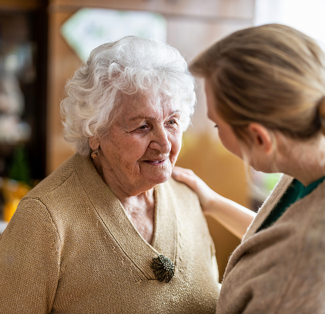 A woman converses with an older woman in a cozy home setting, showcasing a warm and engaging interaction