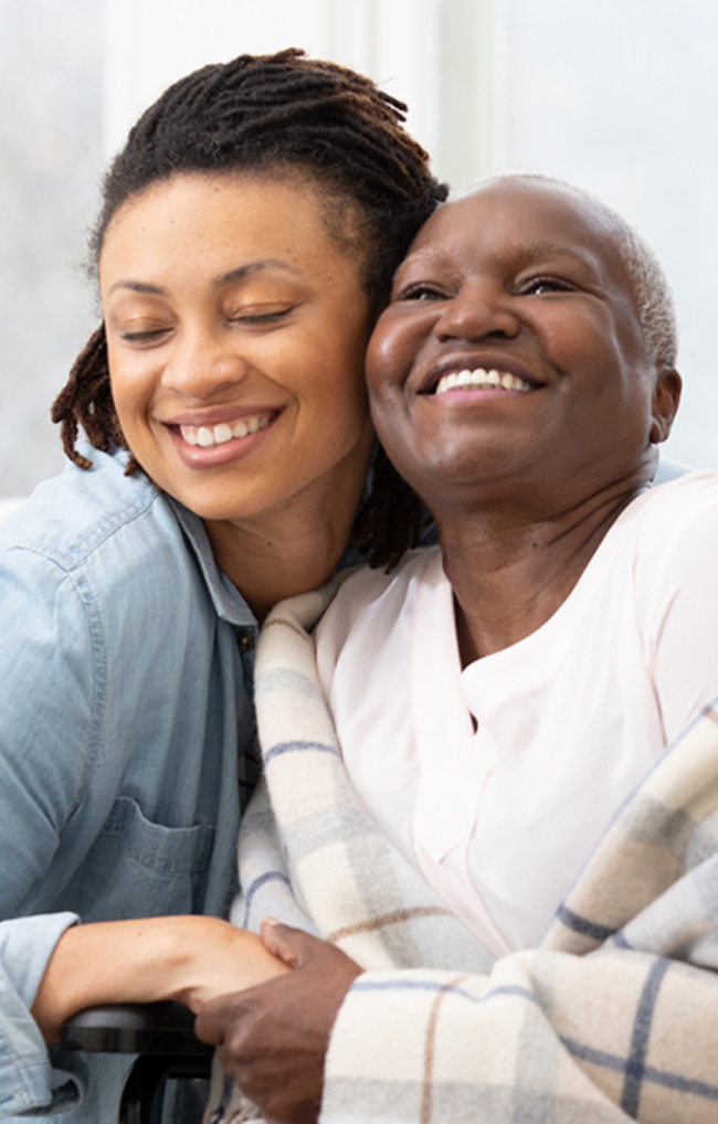 A woman embraces an older woman in a wheelchair, conveying warmth and support in a heartfelt moment