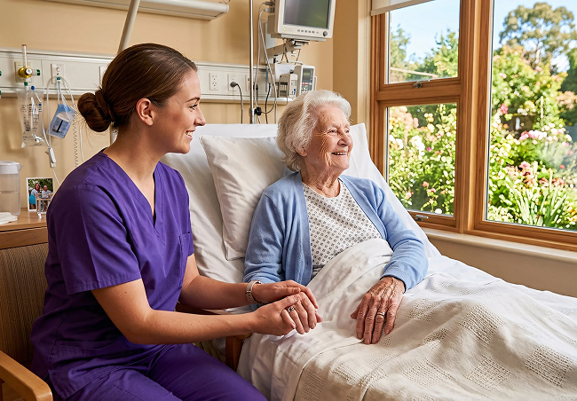 A nurse gently holds the hand of an elderly woman in a hospital bed, providing comfort and support
