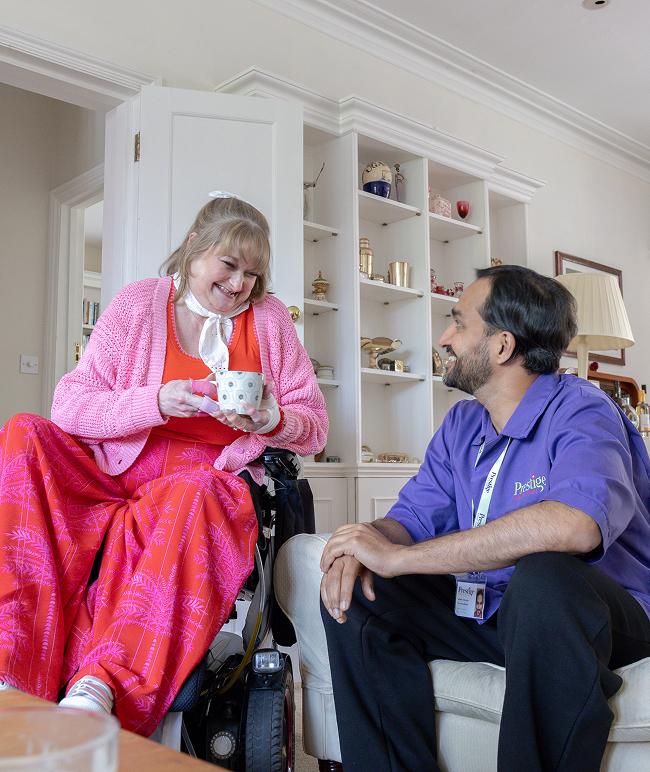 A woman in a wheelchair sits on a couch beside a man, both engaged in conversation and smiling