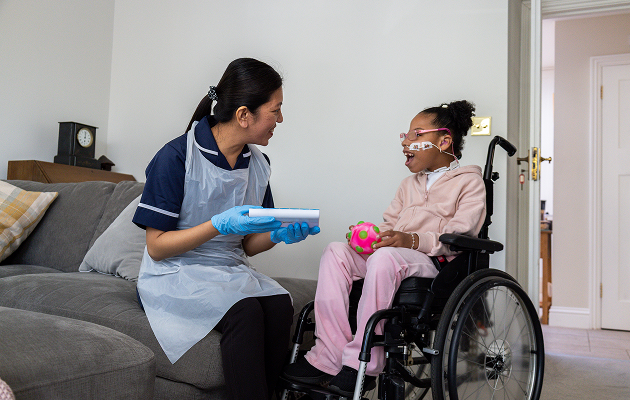 A woman in a wheelchair smiles while holding a child's hand, both enjoying a sunny day outdoors
