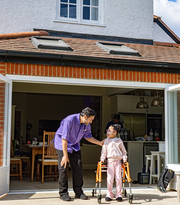 A man and a young girl in a wheelchair are outside a house, enjoying a sunny day together