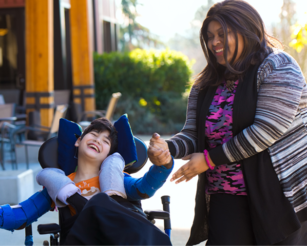 A woman in a wheelchair gently holds a young boy's hand, showcasing a moment of connection and support