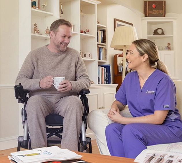 A man in a wheelchair converses with a woman wearing a purple robe, both engaged in a friendly discussion