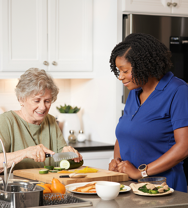 A woman in a blue shirt is slicing a piece of fruit on a cutting board in a kitchen setting