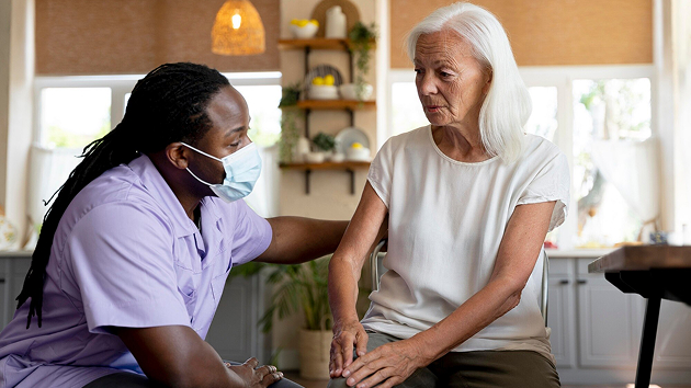 A woman assists an older woman by gently holding her hands, showcasing a moment of support and care