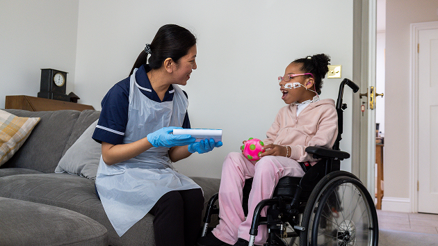 A woman in a wheelchair sits beside a child on a couch, both engaged in a joyful conversation