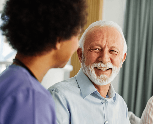 A bearded man and a nurse converse with another man in a medical setting, discussing health-related matters